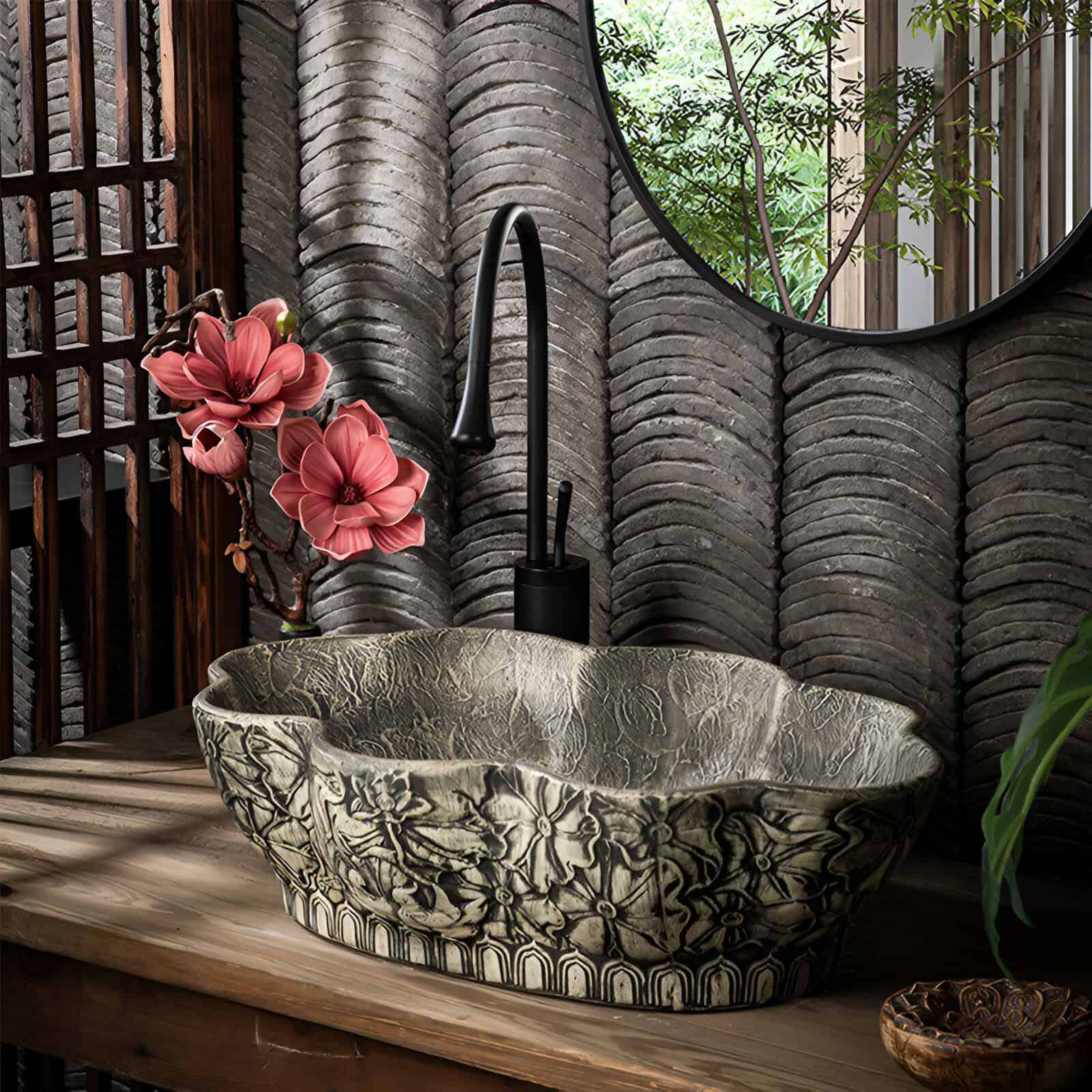 A decorative bathroom sink with carved stone bowl, black faucet, floral arrangement, and natural elements for a luxury spa feel.