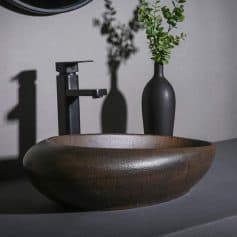 A stylish black sink with a matte finish, paired with a sleek black faucet and minimalist vases with greenery, creating a contemporary and sophisticated bathroom ambiance.