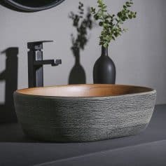 Stylish black faucet with wooden bowl sink and decorative plant vase in contemporary bathroom design.