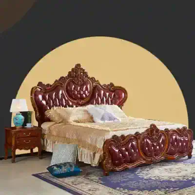 Luxurious bedroom furniture featuring a regal, tufted, burgundy leather bed with ornate carved wooden details, complemented by a vintage side table, stylish lamp, and plush bedding.