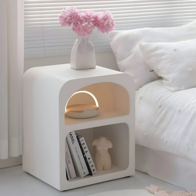 A sleek white bedroom nightstand with a minimalist design, featuring decorative books, a small statue, a warm light, and a vase with pink flowers, perfect for stylish bedroom interiors.