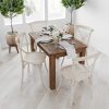 Stylish wooden dining table with white chairs, adorned with fresh flowers, in a bright, modern room featuring potted greenery for a cozy dining ambiance.