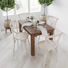 Stylish wooden dining table with white chairs, adorned with fresh flowers, in a bright, modern room featuring potted greenery for a cozy dining ambiance.