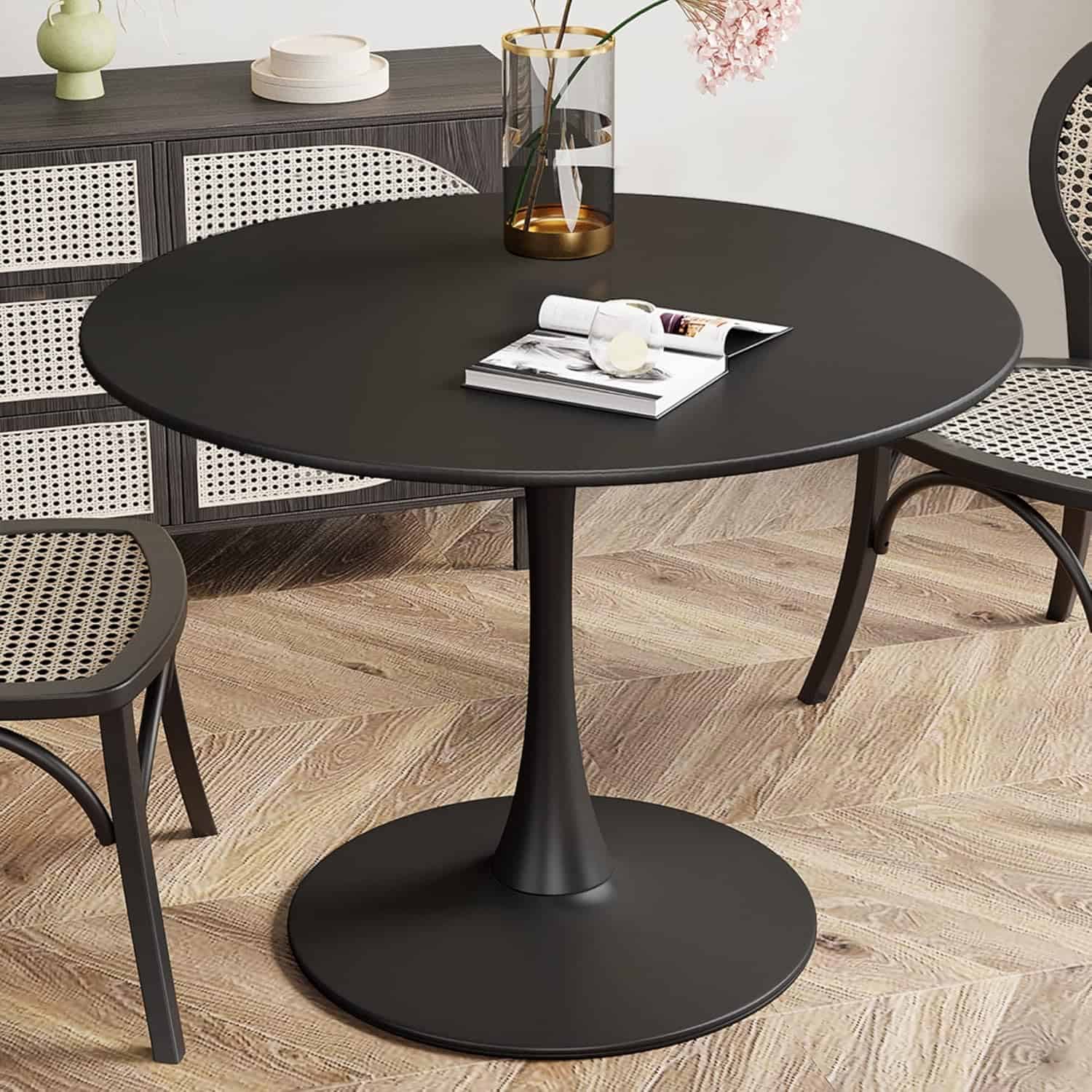 Elegant black round dining table with sleek design, paired with rattan chairs, decorated with a glass vase and books for a sophisticated dining area.