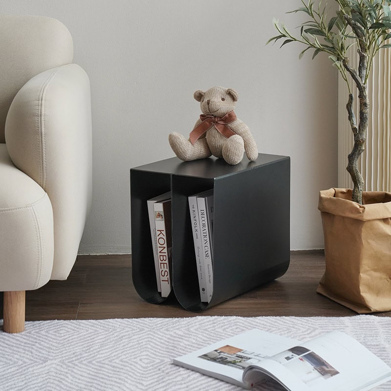 Teddy bear on black side table with books, cozy living room setup, modern interior design with plants, ideal for home decor and furniture shopping, emphasizing comfort and style.
