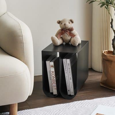 A stylish black optical display stand holding ophthalmology books, topped with a cute teddy bear, situated next to a white sofa in a cozy, modern living space.