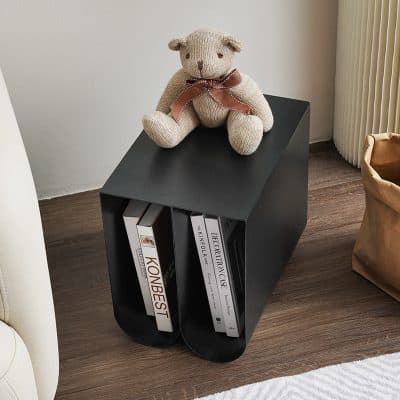 Cute beige teddy bear with a brown ribbon sitting on a sleek black side table holding bestselling books, perfect for cozy home decor and enhancing living room aesthetics.