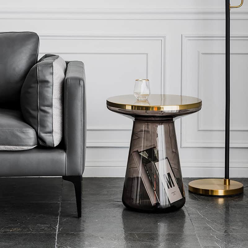 Stylish semi-transparent side table with a gold top, paired with a cozy gray sofa, set in a sleek living space with white wall paneling and a gold-accented floor lamp, perfect for contemporary decor.