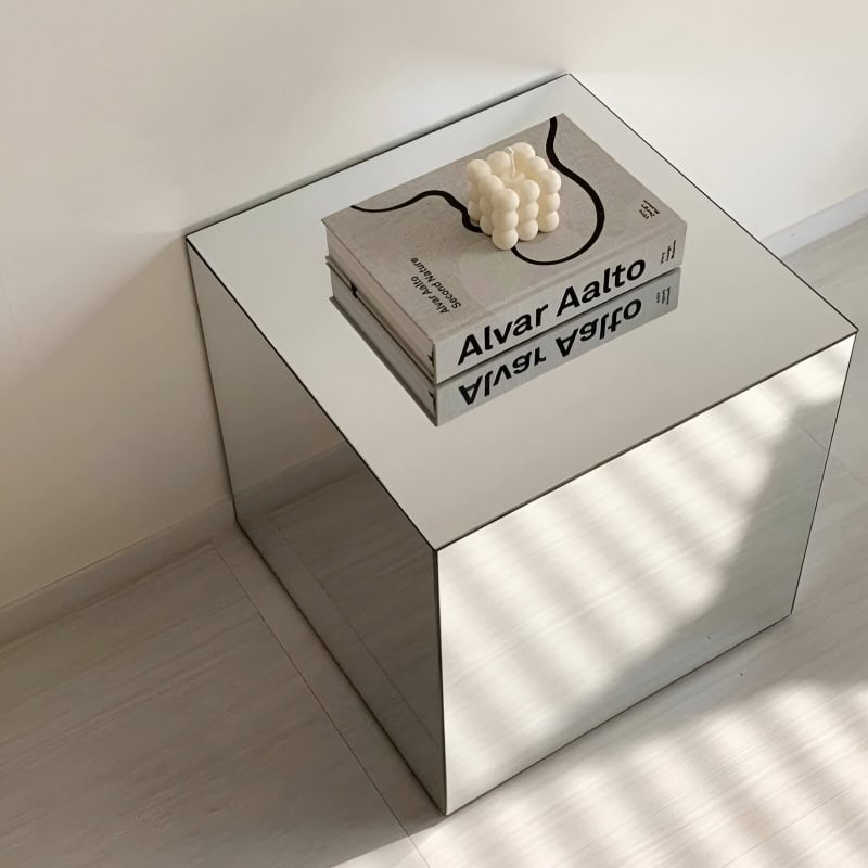 Elegant reflective surface table featuring a book titled "Alvar Aalto" and decorative white candles, ideal for modern interior decor focusing on aesthetic and functional design.