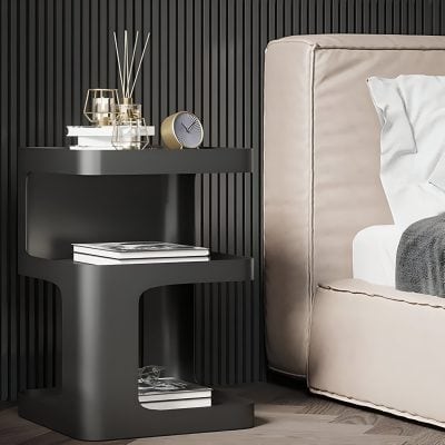 Elegant black side table with accessories including a clock, books, and decorative vases, placed beside a beige upholstered bed in a contemporary bedroom interior.