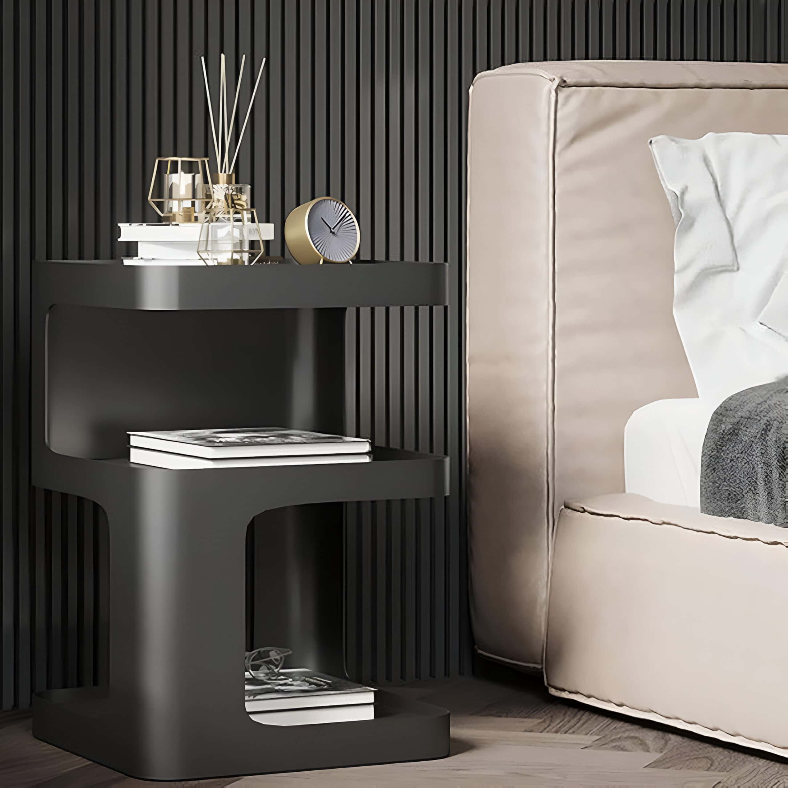 Elegant black side table with accessories including a clock, books, and decorative vases, placed beside a beige upholstered bed in a contemporary bedroom interior.