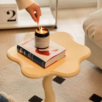 Bright candle on decorative cream-colored side table with elegant curves, ideal for relaxation and creating a calming atmosphere in a contemporary bedroom.