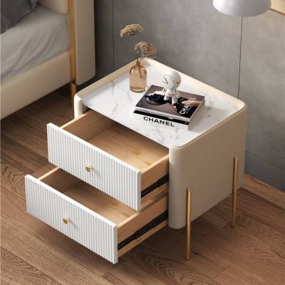 Stylish bedroom nightstand featuring two open drawers, a marble top, and elegant accessories including a Chanel magazine and a small sculpture.