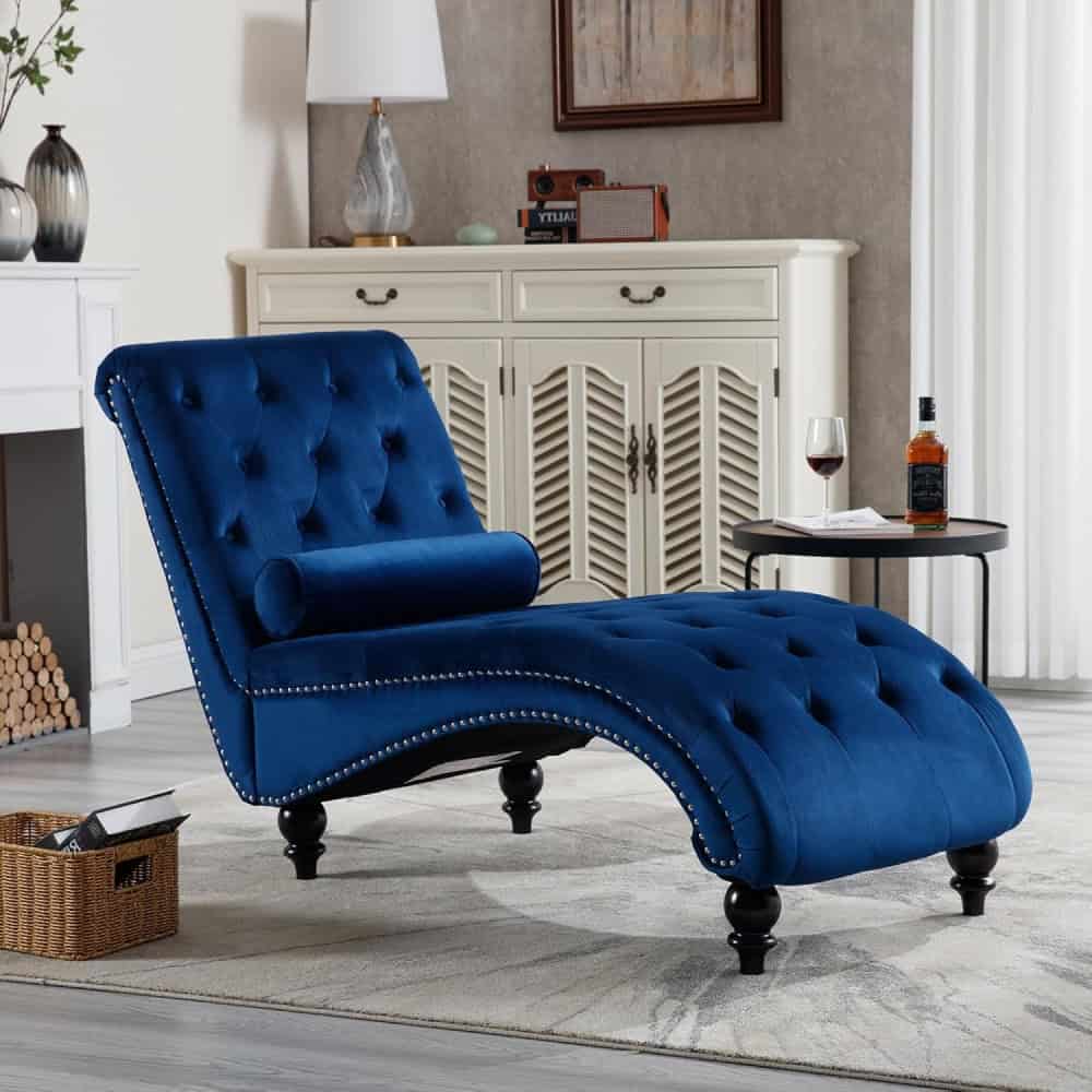 Elegant blue velvet chaise lounge with tufted design, nailhead trim, and rolled bolster cushion perfect for stylish living rooms and modern decor.