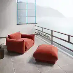 Relaxing living space with stylish red armchair and ottoman overlooking the sea, perfect for outdoor relaxation and enjoying scenic ocean views.
