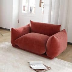 Comfortable plush red armchair in a bright living room with large windows, ideal for relaxation and reading. Perfect addition to modern home decor; enhances interior comfort and style.