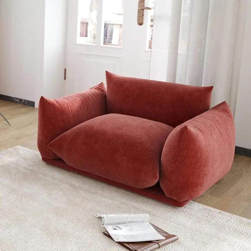 Comfortable plush red armchair in a bright living room with large windows, ideal for relaxation and reading. Perfect addition to modern home decor; enhances interior comfort and style.