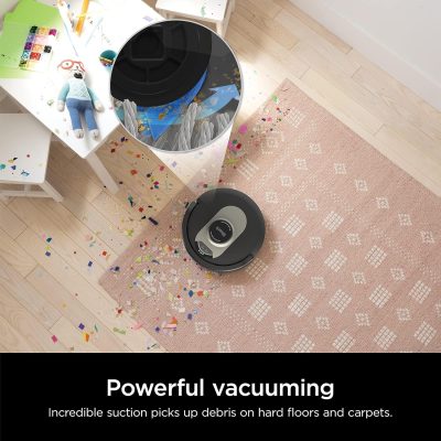 Vacuum cleaner cleaning a pink patterned rug with colorful confetti on hardwood floor in a modern living space.