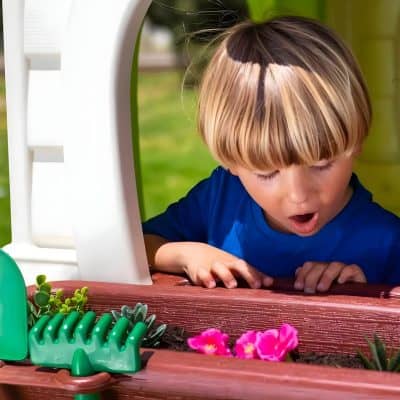 Children exploring outdoors in a garden with gardening tools and flowers.