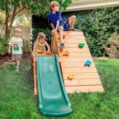 Colorful backyard playground with a slide and climbing wall, surrounded by lush greenery, children playing and having fun, promoting outdoor activities and family entertainment.