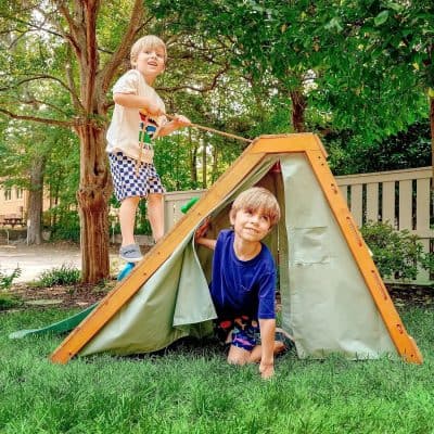 Kids playing with a tent outdoors in a lush green backyard, enjoying a fun summer day, representing outdoor recreation, family bonding, and childhood adventure.