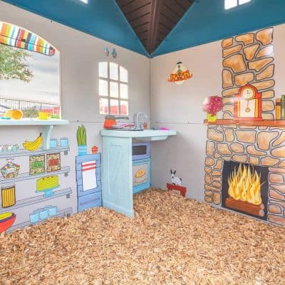Colorful children's playhouse interior with painted kitchen, fireplace mural, and cozy decor at Monalisa Medical Store. Perfect for kids' role play and imaginative fun.