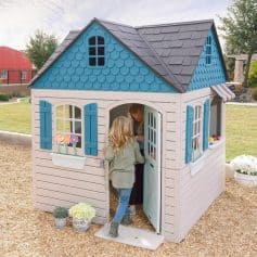 Colorful kids playhouse with blue shutters, window boxes, and a striped awning in a backyard. Perfect for children’s outdoor play and imaginative adventures. Features detailed design and easy access.