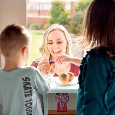 Bright-eyed woman enjoying a colorful pair of toy glasses with children, inside a modern optometry store, showcasing high-quality eyewear and friendly optometry services at Monalisa Store.