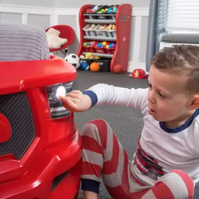 Playful young boy pressing buttons on a red toy car at Monalisa Store, kids' play area with sports balls and toys in the background, encouraging child-friendly environment for children.