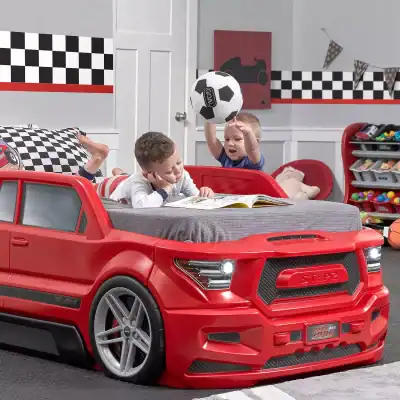 Kids playing in a car-shaped bedroom bed with sports-themed decor, including a soccer ball and racing flags; a fun, playful space for children to relax and enjoy imaginative activities.