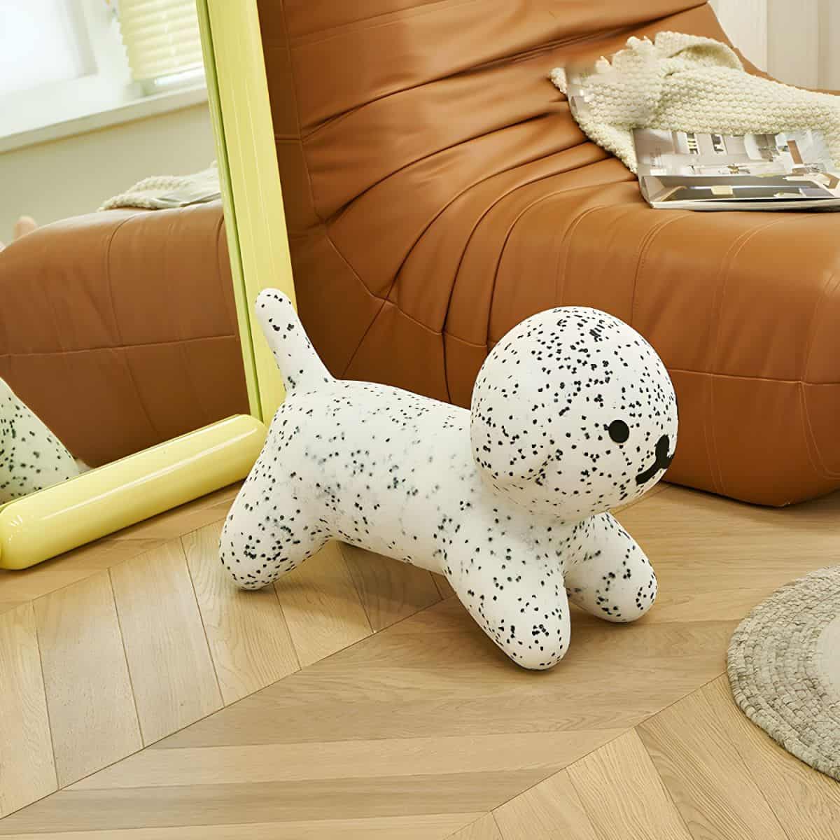 Soft dog plush toy with black speckles on white, placed near a mirror and leather sofa, in a trendy home interior. Perfect for pet lovers and cute home decor accents.