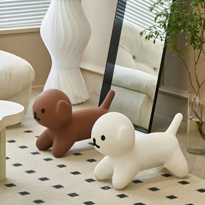 Cute balloon dog toys in white and brown colors placed on a beige rug in a cozy, well-lit room with a full-length mirror, a white sofa, a leafy plant, and stylish decor elements.