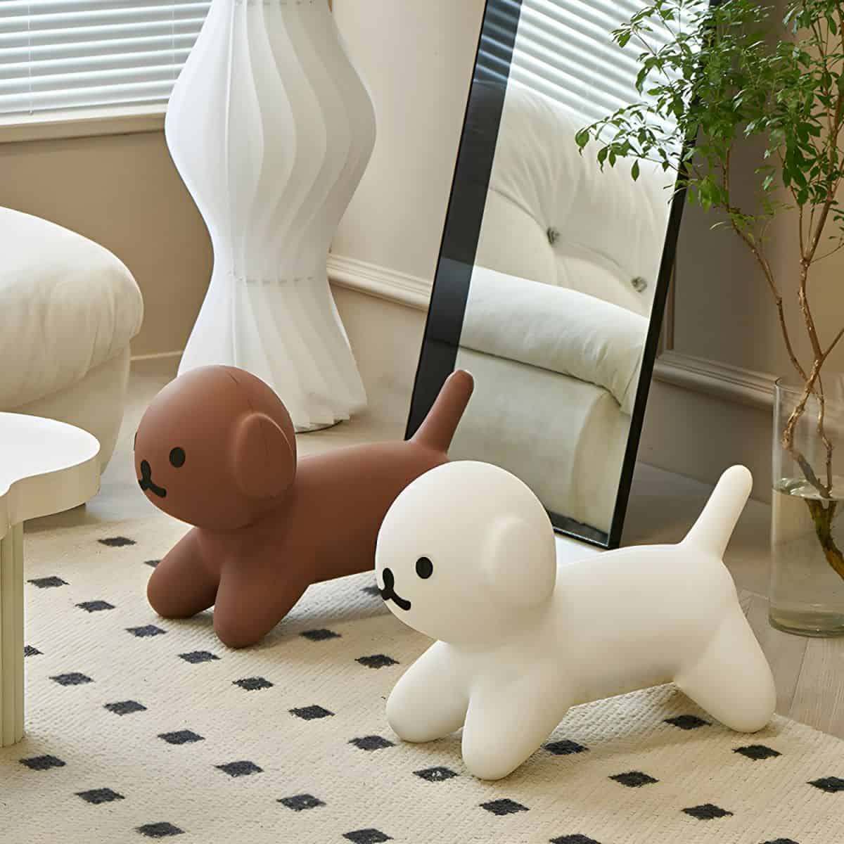 Cute balloon dog toys in white and brown colors placed on a beige rug in a cozy, well-lit room with a full-length mirror, a white sofa, a leafy plant, and stylish decor elements.