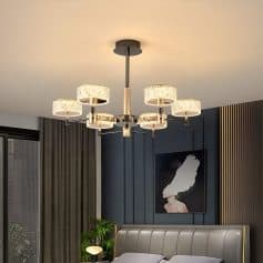Elegant modern chandelier with multiple lampshades hanging above a stylish bedroom with dark blue accent wall and contemporary art.