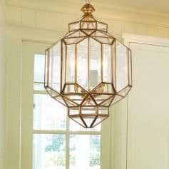 A modern geometric gold chandelier hanging in a bright room with large windows, ideal for elegant interior decor and stylish lighting solutions.