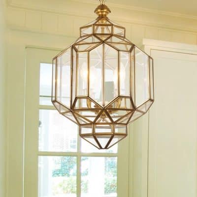 A modern geometric gold chandelier hanging in a bright room with large windows, ideal for elegant interior decor and stylish lighting solutions.