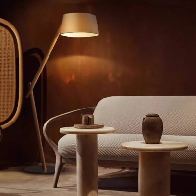 Elegant living room with modern minimalistic furniture and warm ambient lighting, featuring a white upholstered sofa, marble side tables with decorative pottery, and a floor lamp against a dark wall.