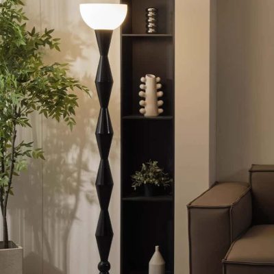 Elegant modern floor lamp with a white lampshade and black geometric stand, next to a potted plant and a stylish black shelving unit with decorative vases, in contemporary Monalisa Store interior design.