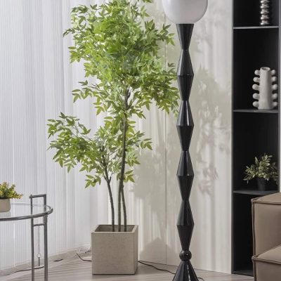Luxury modern floor lamp with black geometric design and white shade in contemporary interior space brightened by green indoor plant of variegated leaves.