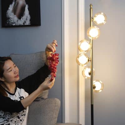 Gorgeous woman holding a bunch of red grapes near a modern floor lamp in a stylish home interior.