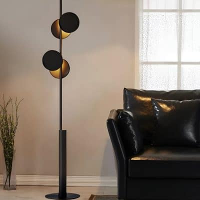 Modern black and gold floor lamp with spherical shades, stylish black leather sofa with cushions, and a decorative vase with dried branches in a contemporary living room setting.