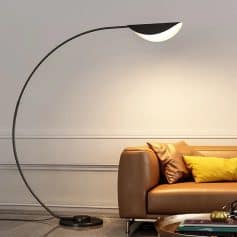 Contemporary floor lamp with a curved black stand and modern moon-shaped light, positioned next to a stylish brown leather sofa with yellow and bronze pillows in a modern living room.
