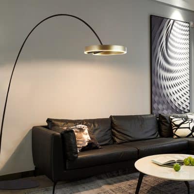Modern black leather sofa with decorative pillows in a stylish living room featuring contemporary art and a unique arc floor lamp.