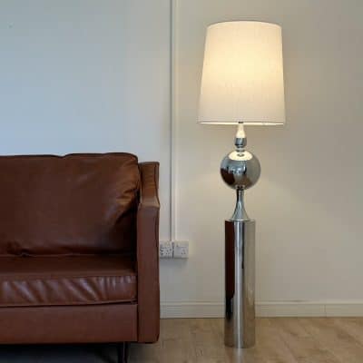 Modern floor lamp with a shiny metallic base and white lampshade in living room, minimalist interior decor.