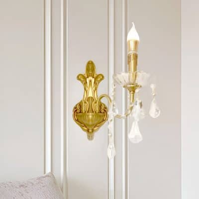 Golden ornate wall sconce with crystal accents and a candle-shaped lightbulb, elegant interior decor for luxury space.