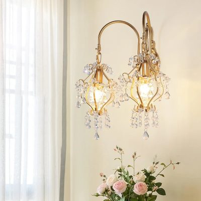 Intricate gold and crystal wall sconce with elegant hanging prisms, adorned with fresh pink roses below, perfect for enhancing luxurious interior decor in a sophisticated setting.