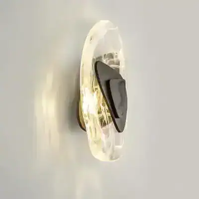 Illuminated modern wall light fixture with a clear glass sculpture and a black metal base, perfect for enhancing contemporary interior decor in living rooms or bedrooms.