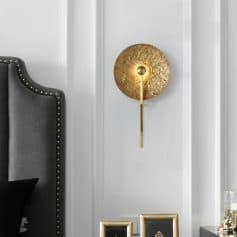Shining gold modern wall sconce with textured disc design, perfect for luxurious bedroom or living room decor. Elegant lighting fixture enhances interior aesthetics.