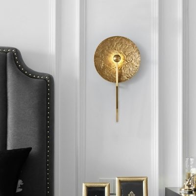 Shining gold modern wall sconce with textured disc design, perfect for luxurious bedroom or living room decor. Elegant lighting fixture enhances interior aesthetics.