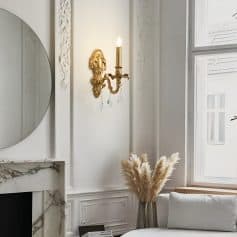 Elegant interior with ornate wall sconce, decorative mirror, marble fireplace, and cozy seating area featuring pampas grass decor, highlighting sophisticated home aesthetic and luxurious design.